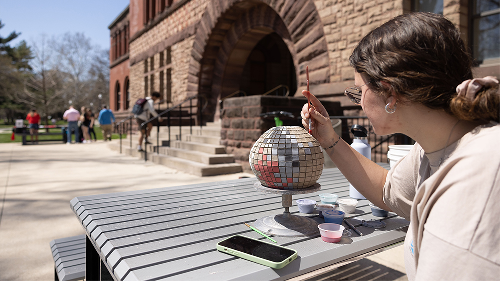 A student paints on an art project outside of Hayes Hall on a warm spring day.