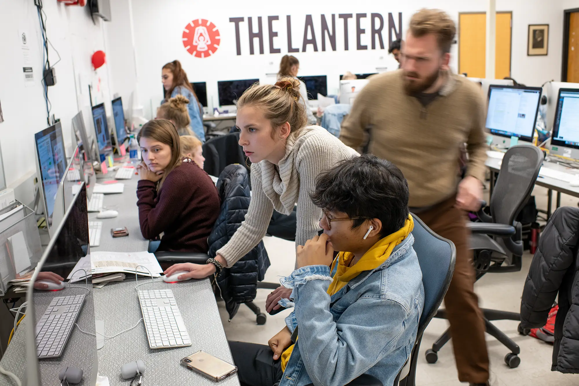 Several students and an advisor gather around a computer in The Lantern's office.