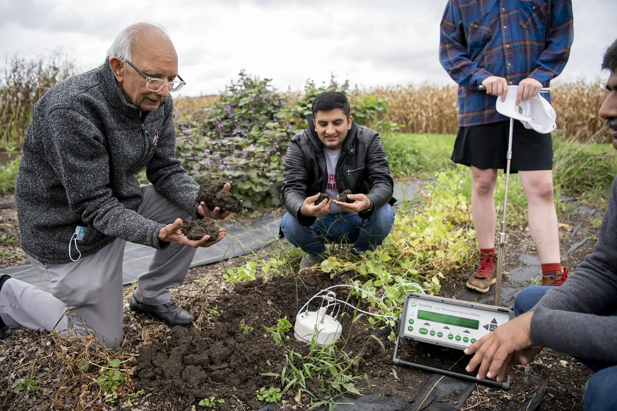 Professor Rattan Lal kneels in an agricultural field alongside three students and soil testing equipment.