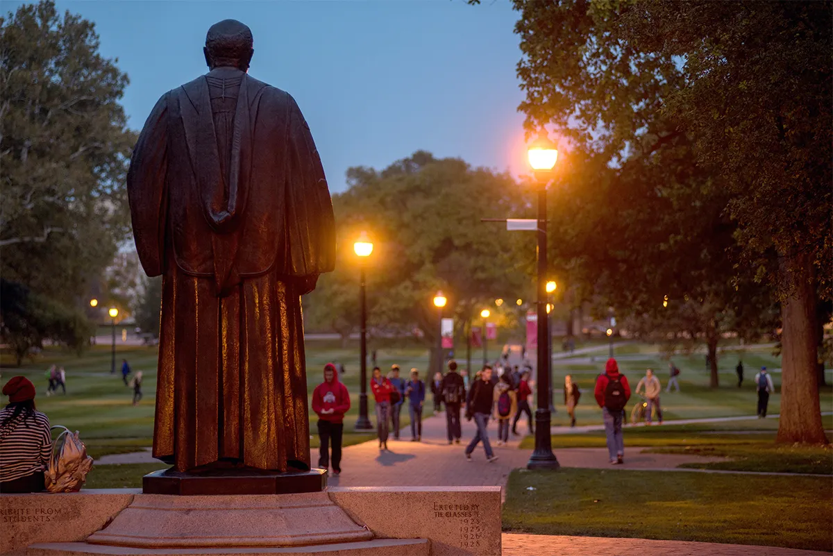 Students walk on the Oval with the statue of William Oxley Thompson in the foreground.